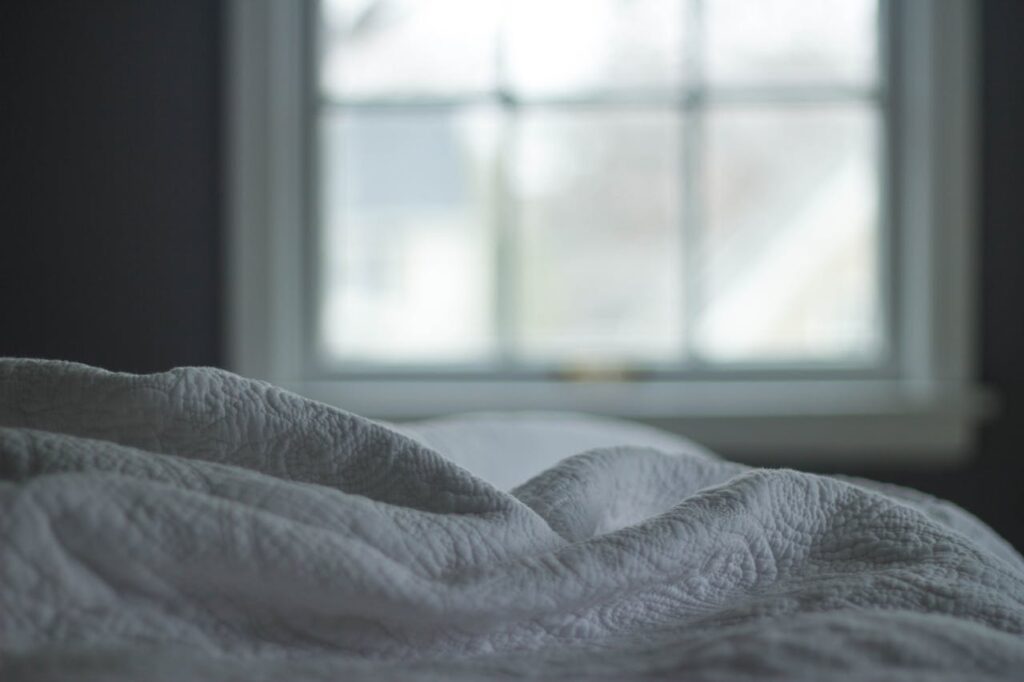 pexels-photo-57686 A tranquil bedroom view with a quilted blanket by the window softly lit by morning light, ideal for relaxation themes.